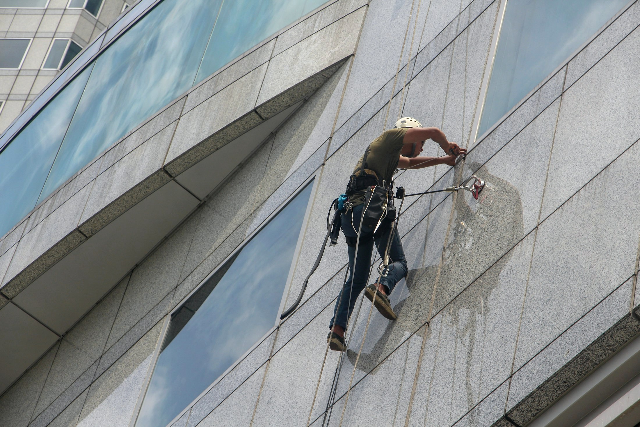 Vitrier professionnel lavant une grande façade vitrée, suspendu sur corde